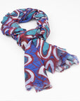 Kirrikin Wildflowers Luxury Cashmere Scarf styled in a loose knot, featuring bold blue, turquoise, red, and white circular Indigenous artwork by Carol Martin.