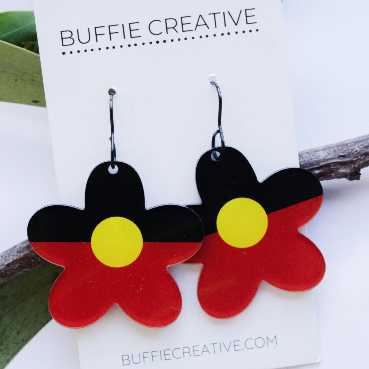 Aboriginal Flag Flower Earrings on Buffie Creative card packaging, featuring flower-shaped drops in the black, red, and yellow colours of the Australian Aboriginal flag on dark ear wires, designed by Buffie Punch.