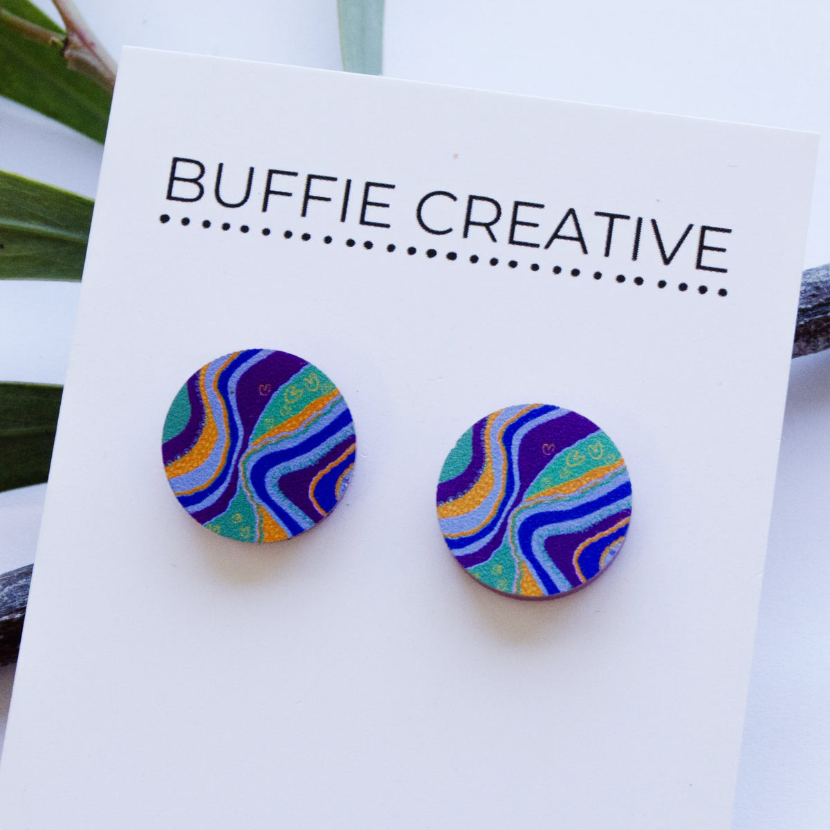 Round Blue Story Stud Earrings on Buffie Creative card packaging, featuring vibrant flowing layers of blue, purple, turquoise, and yellow ochre Indigenous artwork designed by Buffie Punch.