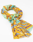 Kirrikin Karijini Luxury Cashmere Scarf styled in a loose knot, featuring vibrant yellow ochre, seafoam green, turquoise, and purple Indigenous artwork by Sally White.