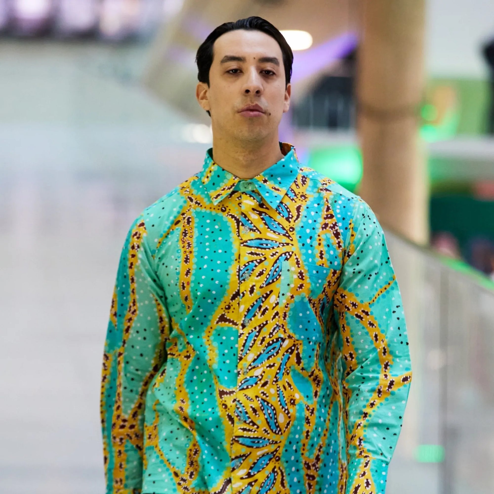 Medium close-up of a male model wearing the Kirrikin Karijini unisex shirt, highlighting the collar structure and vibrant turquoise Indigenous artwork by Sally White.