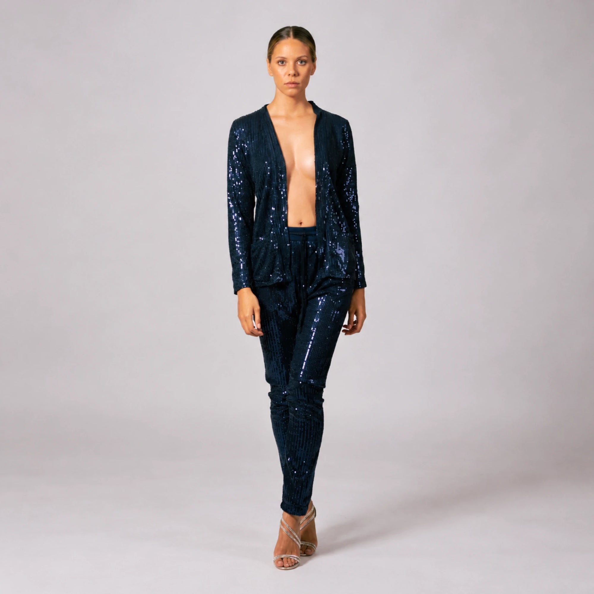 Front view of model wearing navy blue sequin pants paired with a matching blazer suit jacket.