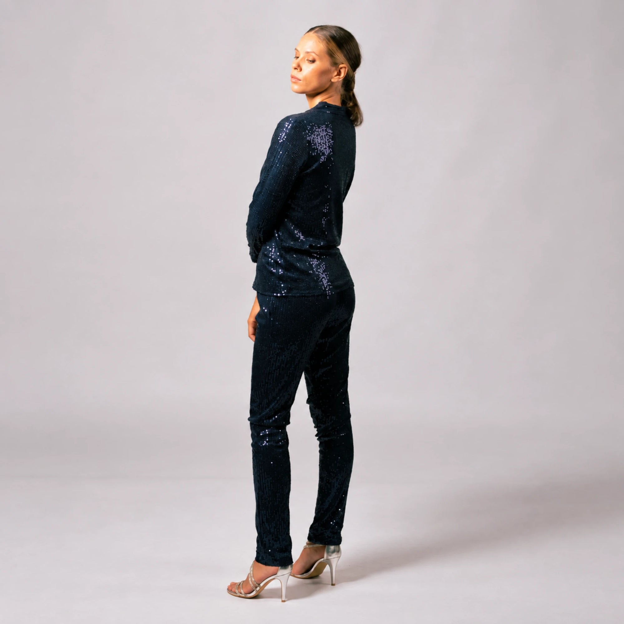 Side and back view of model wearing navy blue sequin pants with a matching sequin jacket.