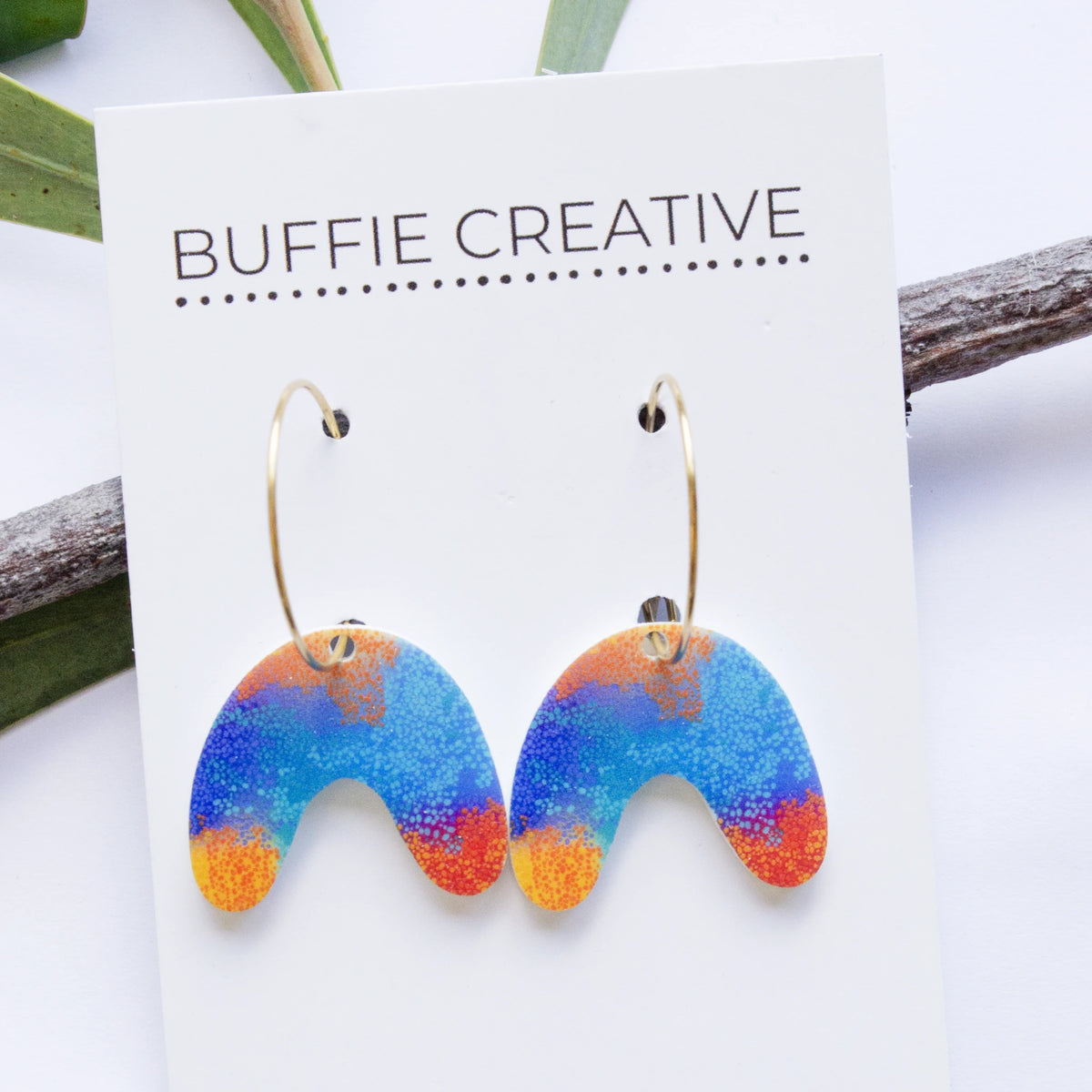 Small U Shape Makuru Earrings on Buffie Creative card packaging, featuring arch-shaped drop charms with vibrant blue, purple, and orange Indigenous dot artwork on gold-toned hoop wires, designed by Buffie Punch.